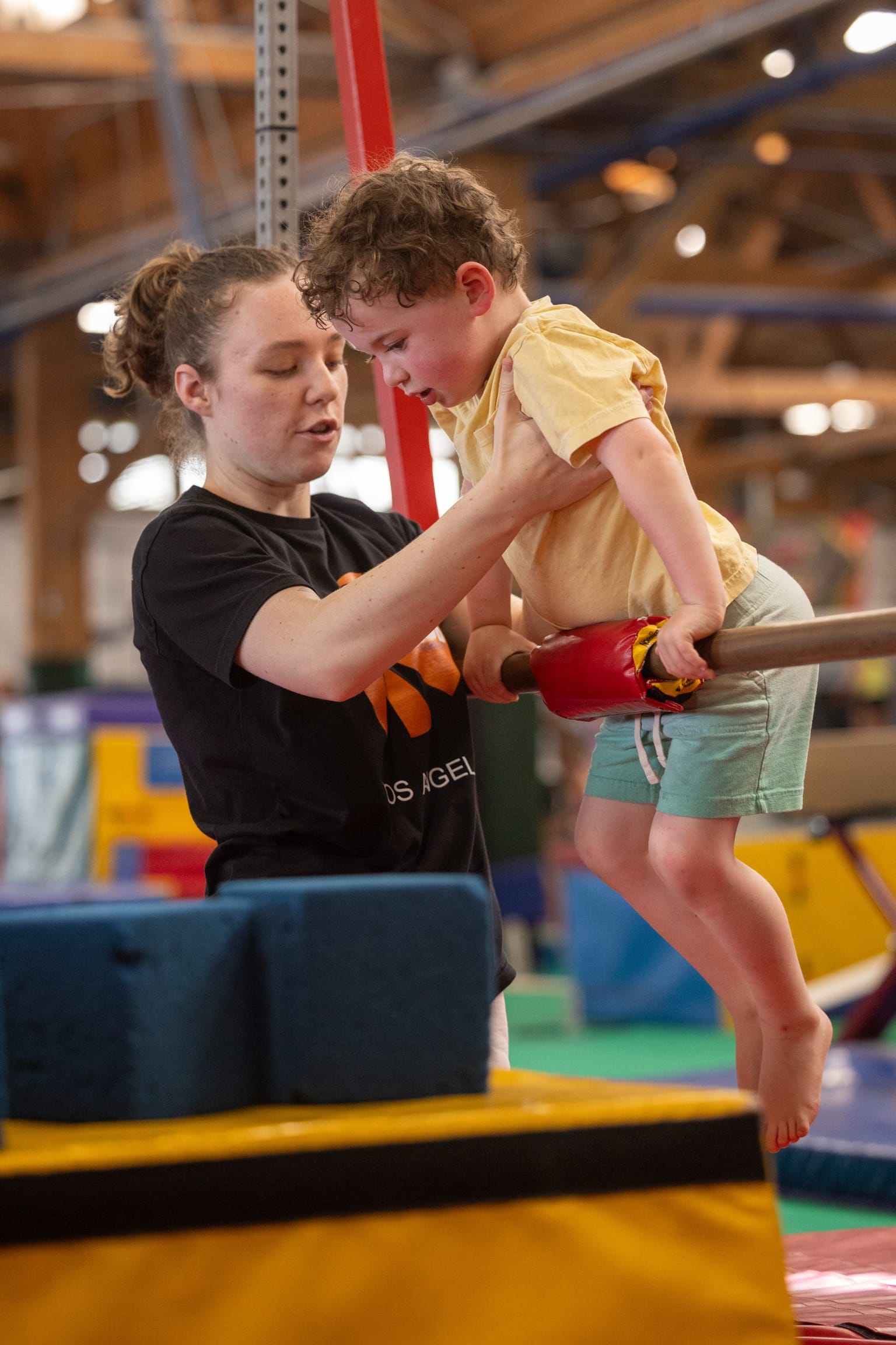A coach helping a young gymnast on a low bar at The Klub
